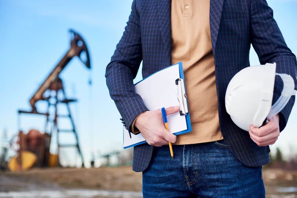 Engenheiro segurando prancheta e capacete de segurança em campo de extração de petróleo.