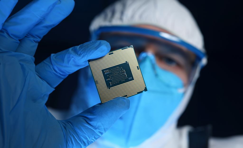 Técnico com luvas e roupa de proteção segurando um microchip para inspeção.
