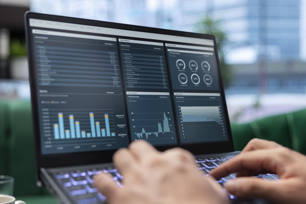 Pessoa usando notebook com dashboards e gráficos de desempenho financeiro na tela, em ambiente corporativo moderno.