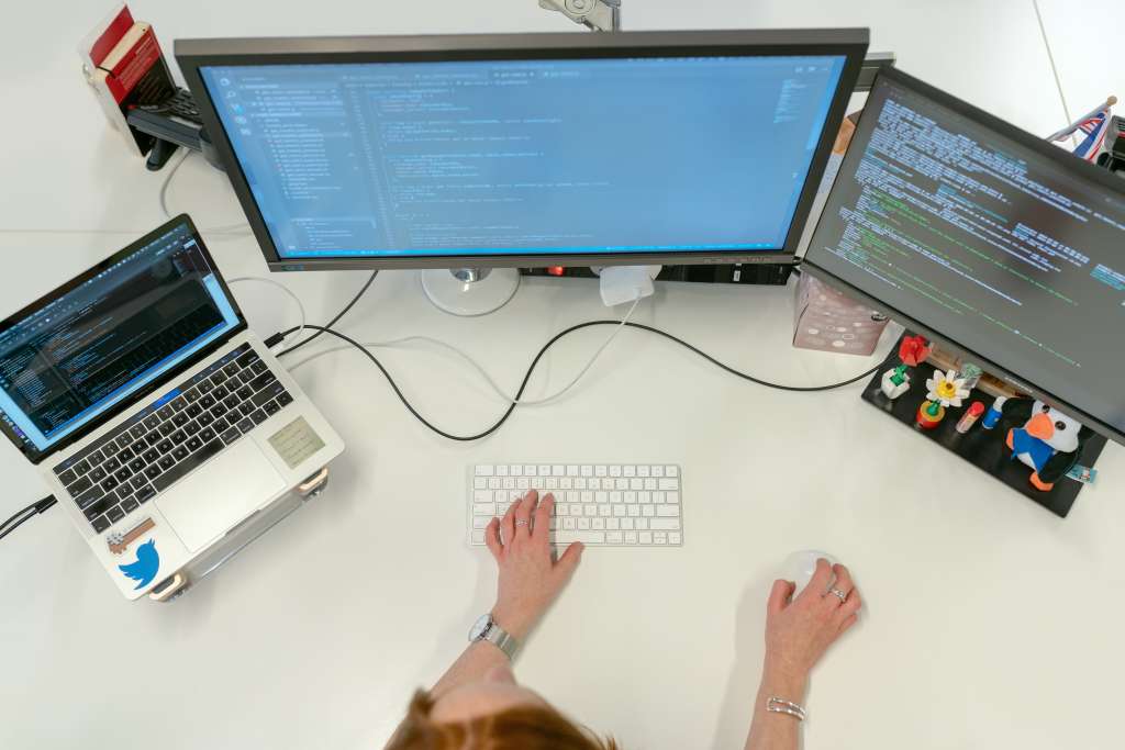 gestor com um notebook e duas telas em frente, com uma mão no teclado e outra no mouse