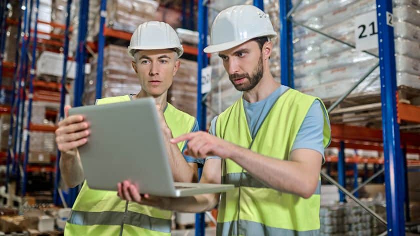 dois homens no chão de fábrica com o notebook na mão analisando os índices