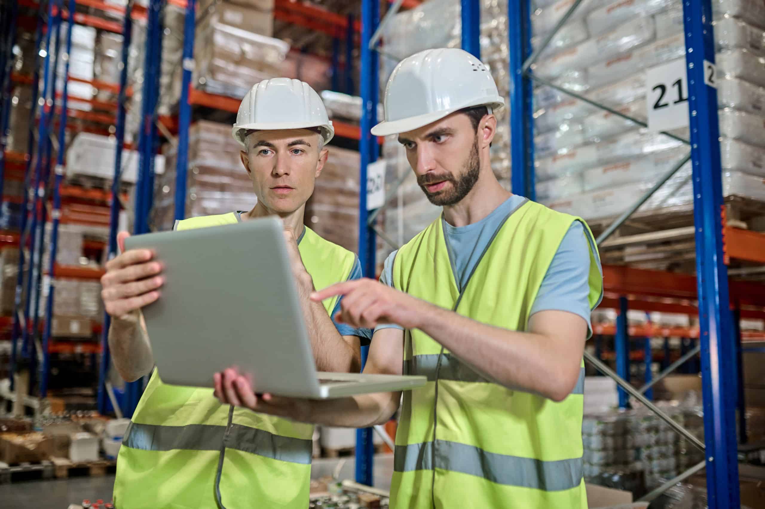 dois homens no chão de fábrica com o notebook na mão analisando os índices