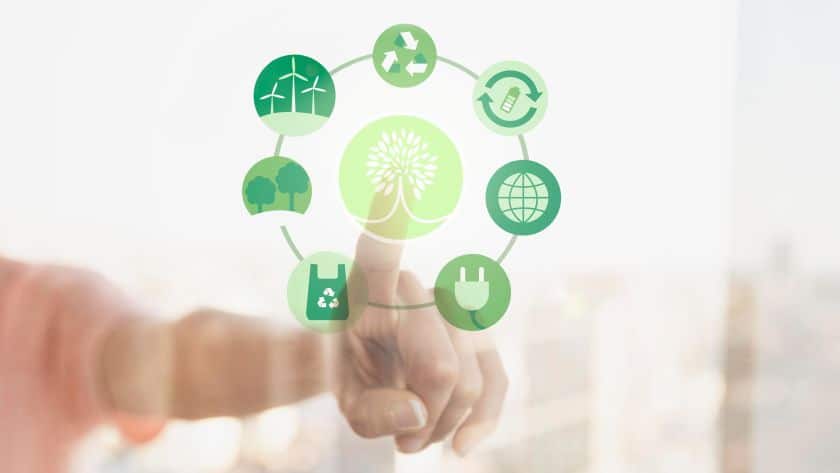 A imagem mostra uma mão tocando uma tela transparente ou interface digital com ícones verdes relacionados à sustentabilidade e gestão ambiental. No centro da composição há um ícone de árvore estilizada, simbolizando o meio ambiente.