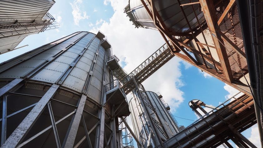 Essa imagem mostra uma visão de silos industriais, com estruturas metálicas que refletem a robustez do setor de armazenamento. O céu claro no fundo contrasta com a complexidade da engenharia das instalações.