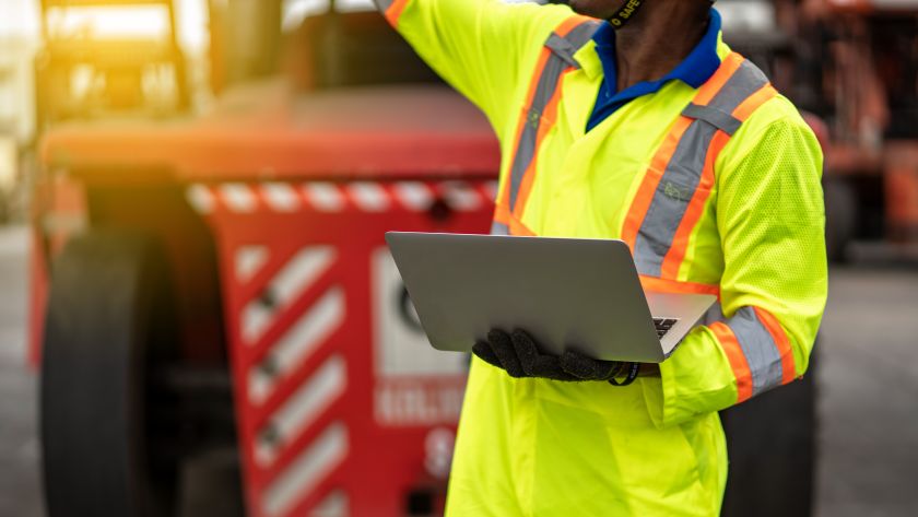 O ChatGPT disse: A imagem mostra um trabalhador vestindo um uniforme de alta visibilidade amarelo com faixas refletivas laranjas e cinzas, típico de ambientes industriais ou de construção. Ele segura um notebook com uma das mãos e parece estar inspecionando ou monitorando algo, com um gesto de apontamento para cima. Ao fundo, há um veículo industrial vermelho desfocado, sugerindo um cenário de logística, construção ou operação portuária. Você sabe quais são as principais normas regulamentadoras que impactam a indústria?