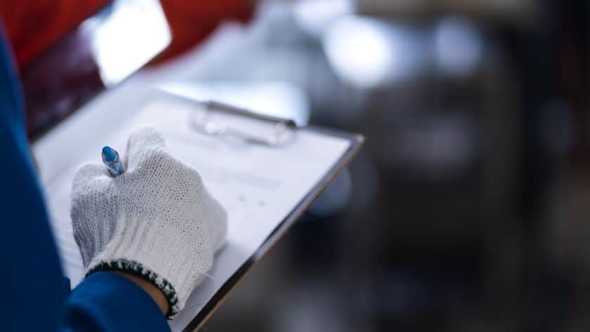Trabalhador com luva de proteção preenchendo formulário em prancheta.
