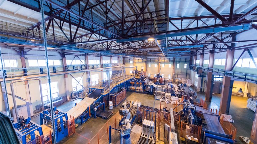 Vista interna de fábrica com esteiras e máquinas industriais em operação.